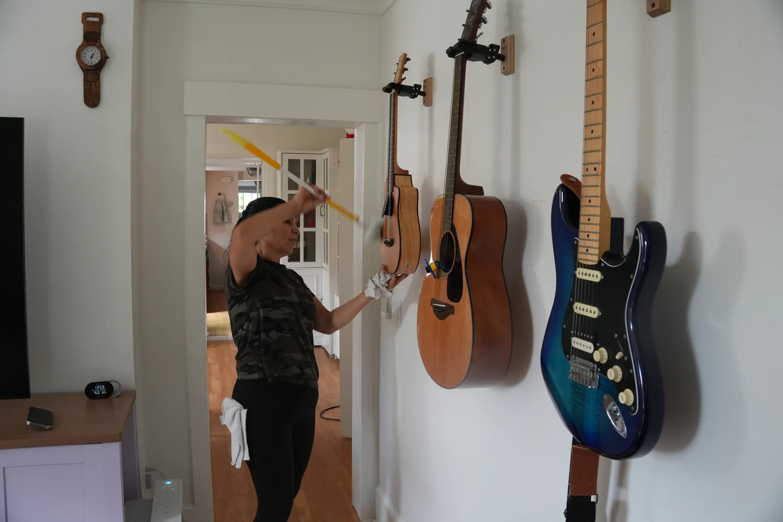 A cleaner dusting a hallway wall beside a row of hanging guitars